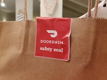 Close-up of a red and white DoorDash branded "safety seal" attached between the handles of a brown p...