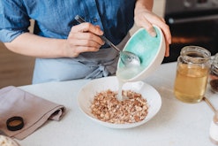 Homemade baked granola: woman adding ingredients into a bowl of rolled oats in the kitchen.