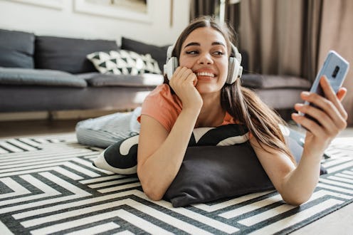 A young woman at home relaxing and listening to some music with headphones while holding a mobile ph...