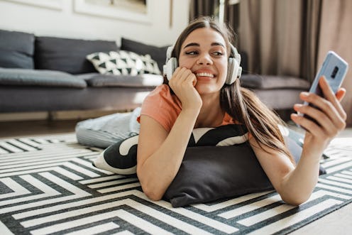A young woman at home relaxing and listening to some music with headphones while holding a mobile ph...