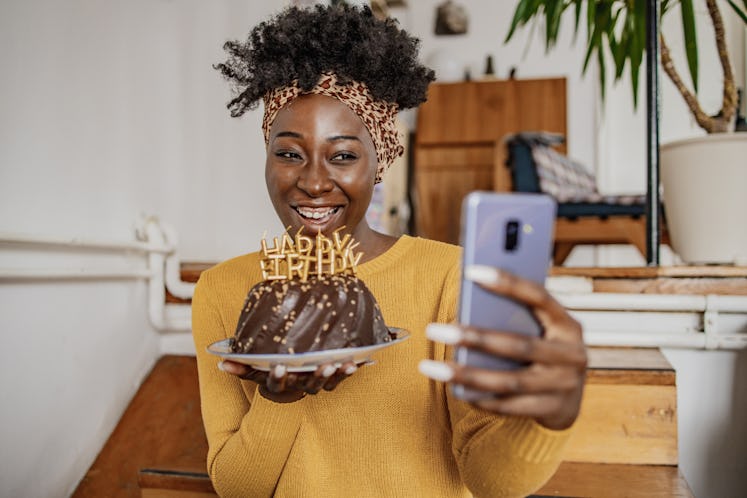 An African-American woman is celebrating a birthday on a video call, she is holding a birthday cake ...