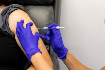 Human hands in protective purple gloves injecting into a persons upper arm, medication That is in a ...