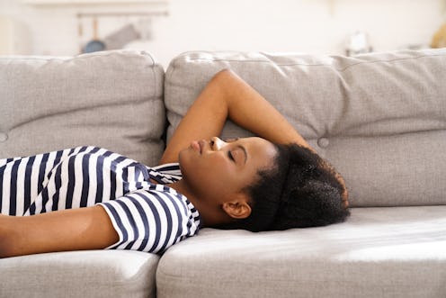 A woman in a striped shirt lies on a couch. These are signs your fatigue might be anxiety-related.