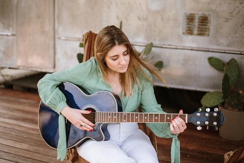 A young woman playing a guitar in a porch of a motor home