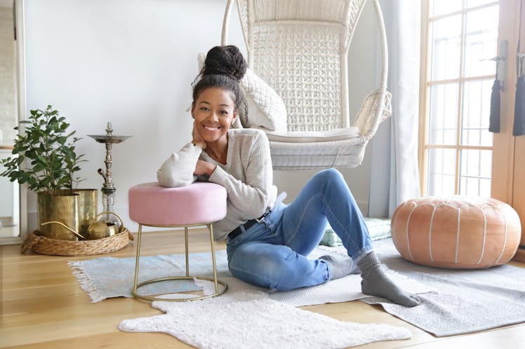 A woman lounges out on the floor at home and leans against a pink stool.