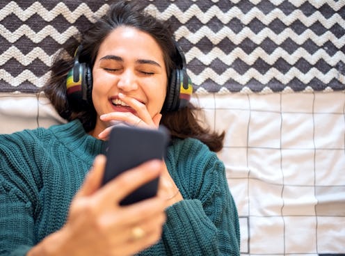 Directly above shot of a young woman watching funny videos on her mobile phone while lying on her be...