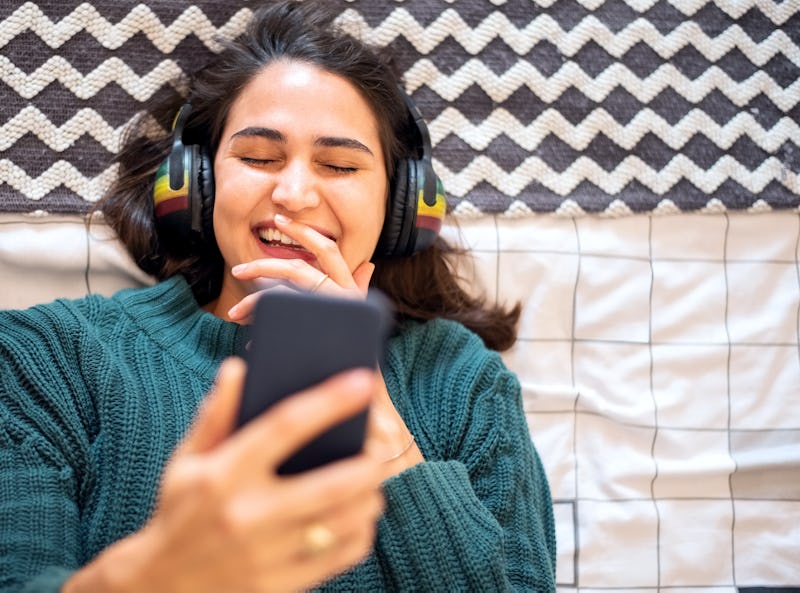 Directly above shot of a young woman watching funny videos on her mobile phone while lying on her be...