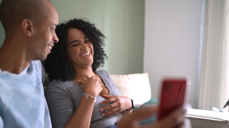 A happy couple laughs while recording a video on their phone.