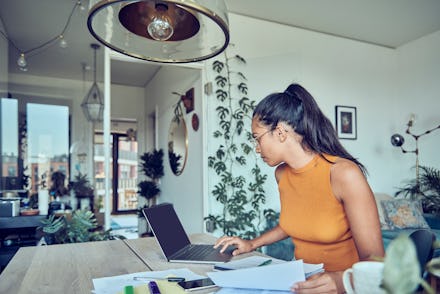 A woman is sitting at a dining table with a laptop and financial statements. Calculates and pays tax...