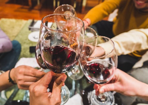 Friends toasting drinks at party. Focus on wineglasses