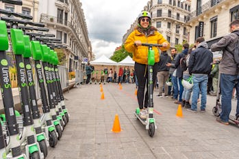 A rider is seen on an e-scooter, passing by a row of Lime scooters. 