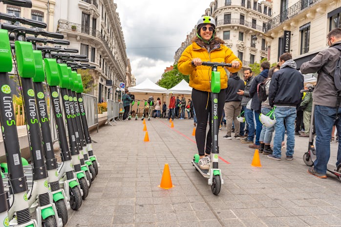 A rider is seen on an e-scooter, passing by a row of Lime scooters. 