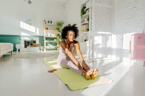 Photo of a young woman practicing yoga in the living room of her apartment; the daily routine of a y...