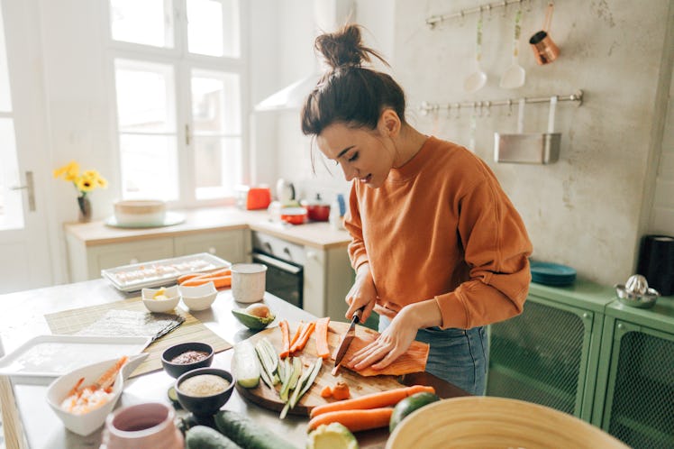 A woman cuts up vegetables to make shrimp sushi rolls.