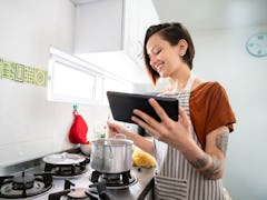 A woman cooks some soup in a pot, while looking at a recipe on her phone. 