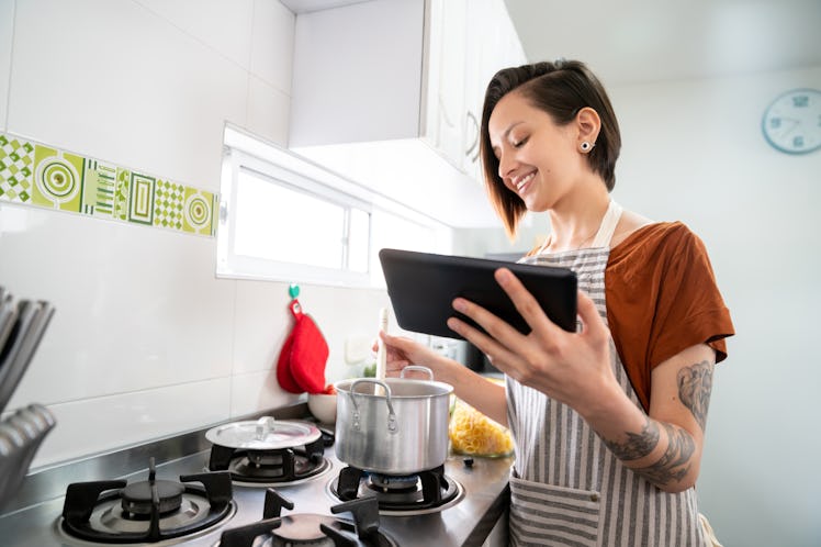 A woman cooks some soup in a pot, while looking at a recipe on her phone.