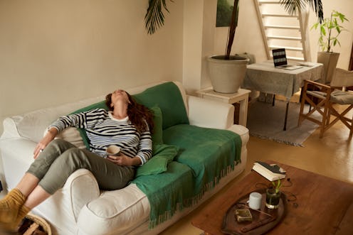 Young woman lying back on a sofa in her living room at home. Doctors explain why getting covid vacci...