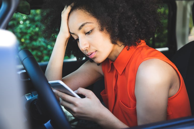 Woman with a orange colored dress pulled over the car and texting on mobile.
