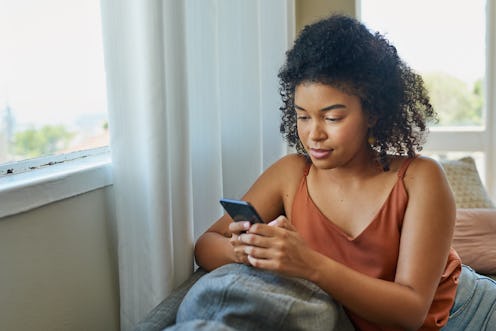 A person with natural hair uses a cellphone while relaxing on a sofa at home. Therapists share what ...