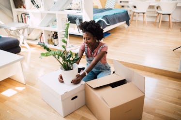 A young woman unpacks a funny planter on Etsy while sitting in her bright apartment.