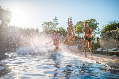 Energetic Spanish friends in 20s and 30s running and jumping into swimming pool at summer social gat...