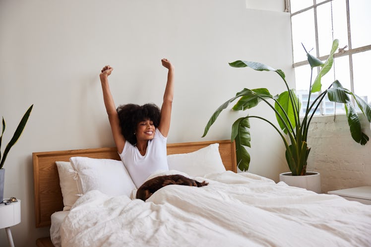 A woman stretches out on her white bed with large windows.