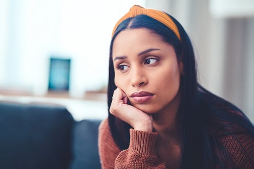 Shot of a young woman looking unhappy on the sofa at home