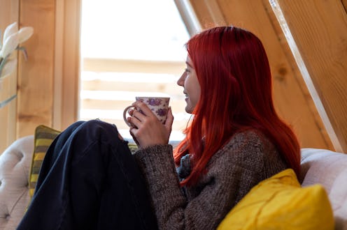 Beautiful young woman reading a book. She sitting on the sofa and holding cup of tea.