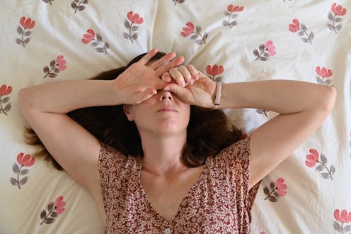 Above view of upset adult woman (age 30-40) lying in bed covering her face.