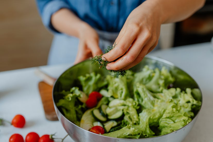 Anonymous woman standing in the kitchen and making a delicious vegetable salad.