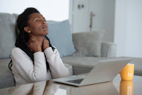 A person massages their own neck while closing their eyes and looking away from their laptop. Fatigu...