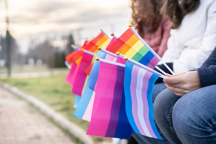 People sitting on a bench holding different flags for the protest defending the LGBTQ rights