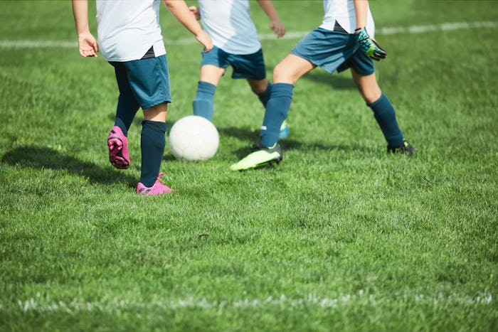 Detail of children's feet on a soccer field with grass on the foreground as copy space.