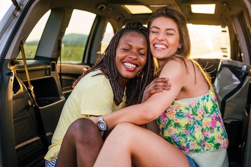 Two females, different nationalities, sitting embraced in the back of the car. They are smiling with...