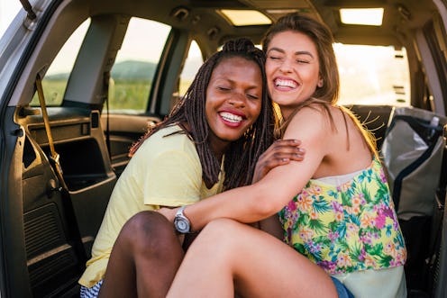 Two females, different nationalities, sitting embraced in the back of the car. They are smiling with...