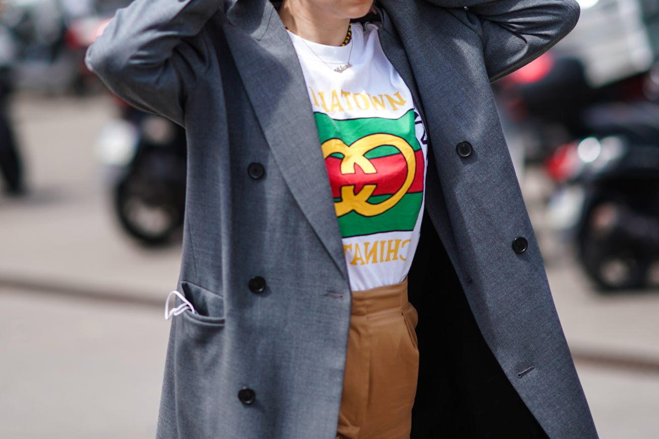 PARIS, FRANCE - JUNE 19: A guest wears a grey trench coat, a white t-shirt with a colorful logo and ...