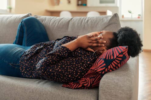 Upset depressed young african american woman lying on couch feeling strong headache migraine, sad ti...