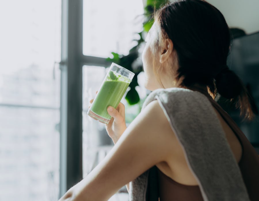 Young Asian sports woman taking a break, refreshing with healthy green juice after fitness work out / exercising / practicing yoga at home in the fresh bright morning