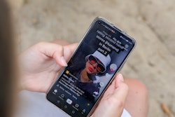 A girl is holding a smartphone in her hands, which shows a video on the TikTok app, she is customizi...