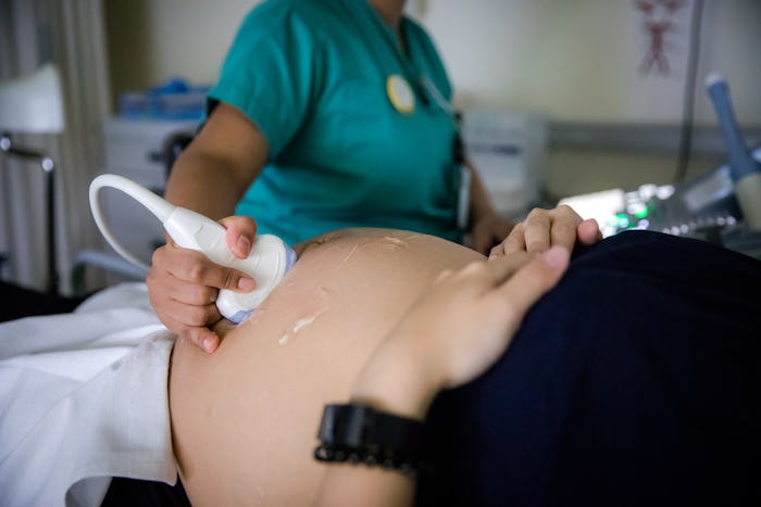 A pregnant woman is lying down on a hospital bed while getting an ultrasound procedure to check the ...