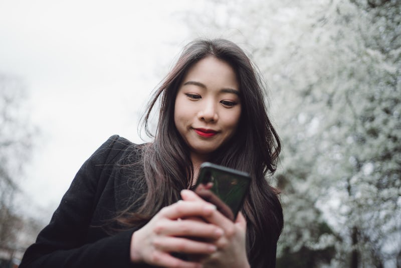 Asian young cheerful woman using smart phone at the park in springtime.