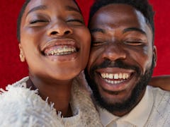 Smiling male and female friend with eyes closed against red wall