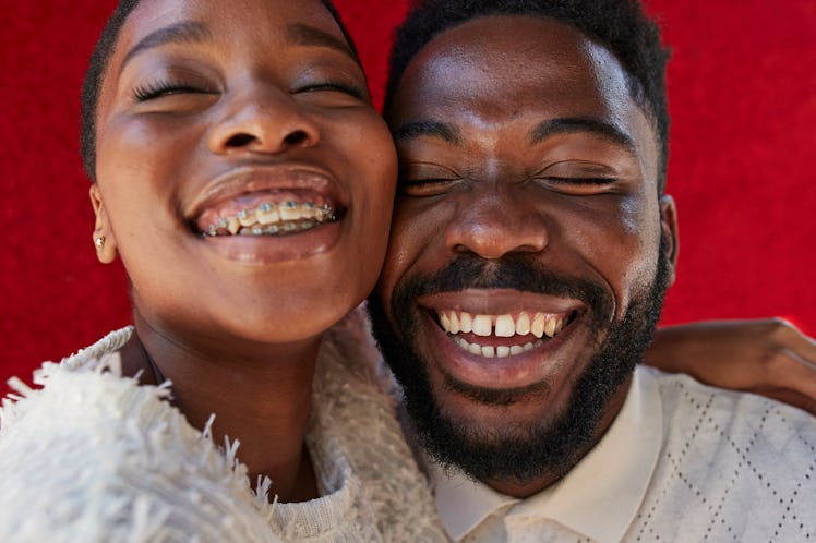 Smiling male and female friend with eyes closed against red wall
