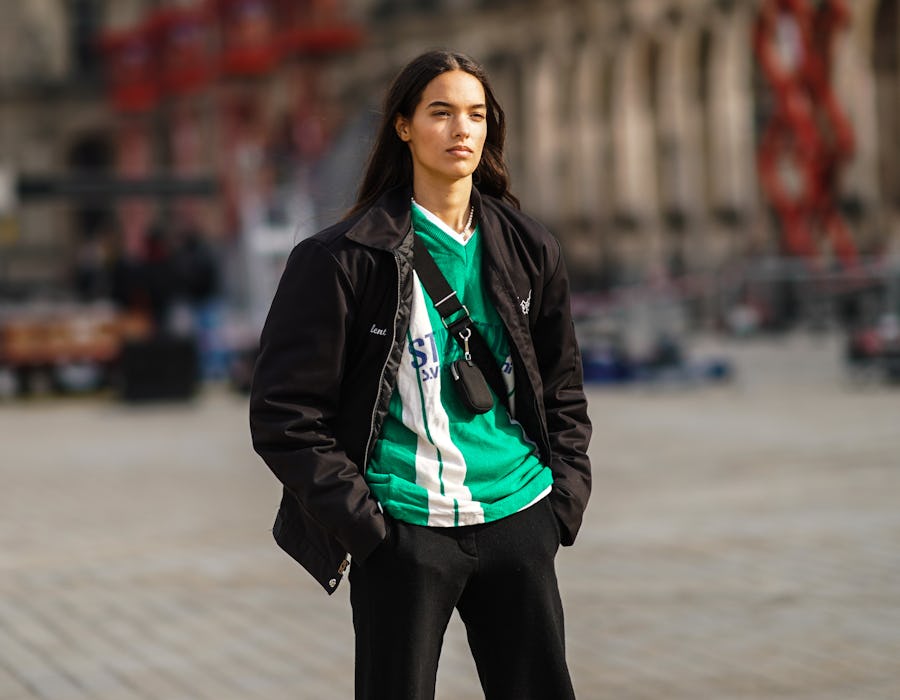 PARIS, FRANCE - MARCH 09: A model wears a a black jacket, a green and white stripe v-neck soccer t-shirt, a mini fanny pack bag crossbody, black pants, on March 09, 2021 in Paris, France. (Photo by Edward Berthelot/Getty Images)