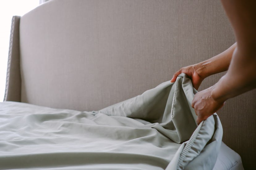 Close-up of unrecognizable woman putting freshly laundered sheet on bed