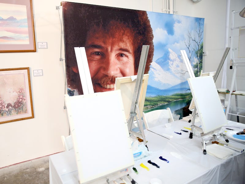 A large sized painting of Bob Ross is seen in a studio.