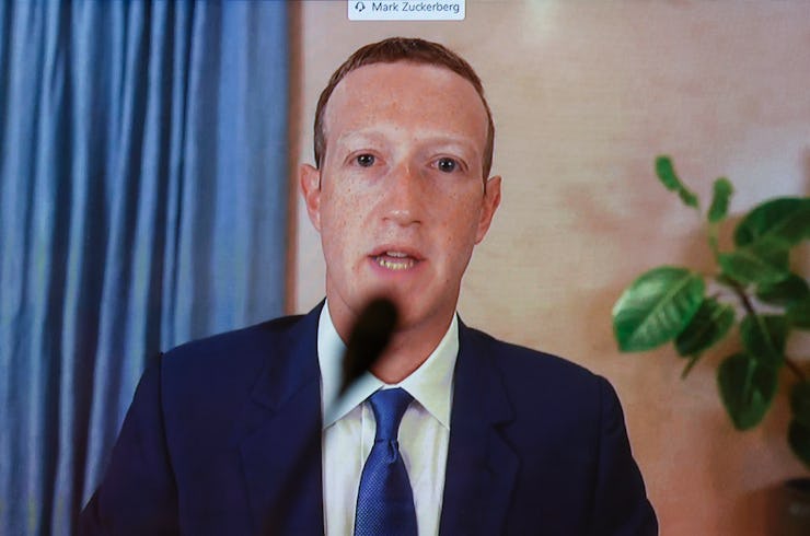 Mark Zuckerberg in a navy suit, a white shirt and a blue tie speaking with a microphone in front of ...
