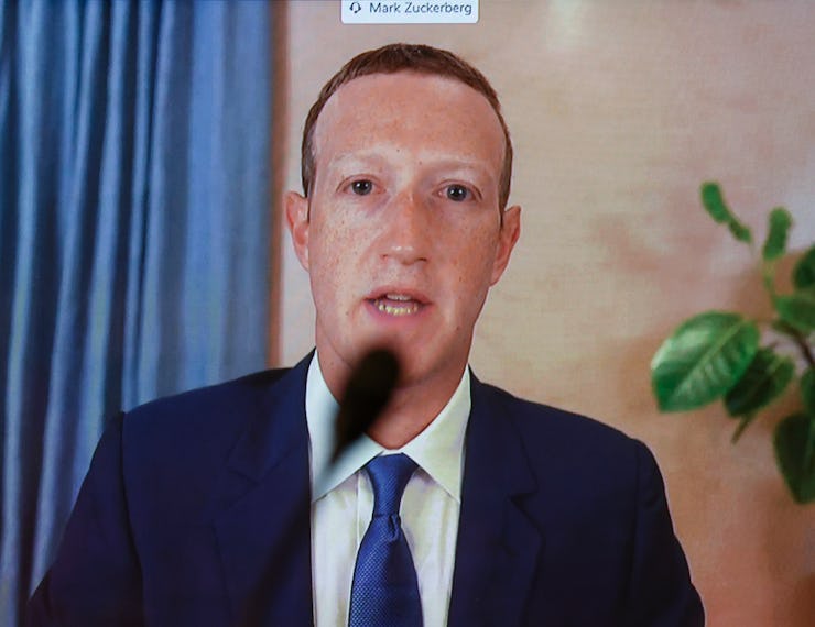 Mark Zuckerberg in a navy suit, a white shirt and a blue tie speaking with a microphone in front of ...