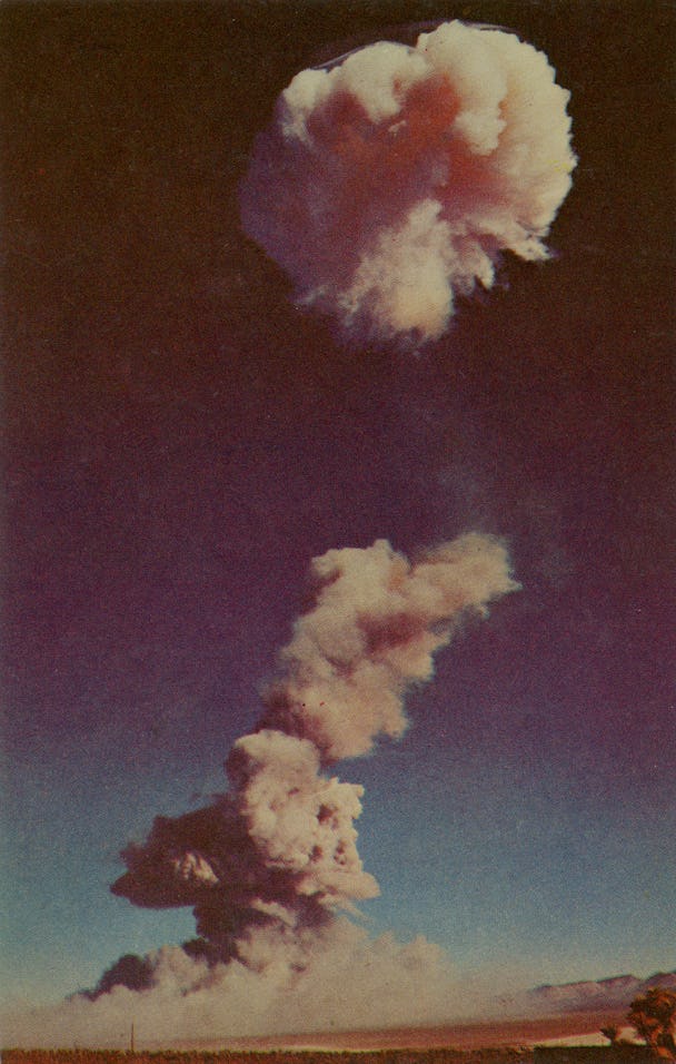 A photographic postcard shows an atomic cloud dissipating over an atomic detonation area, circa 1952...