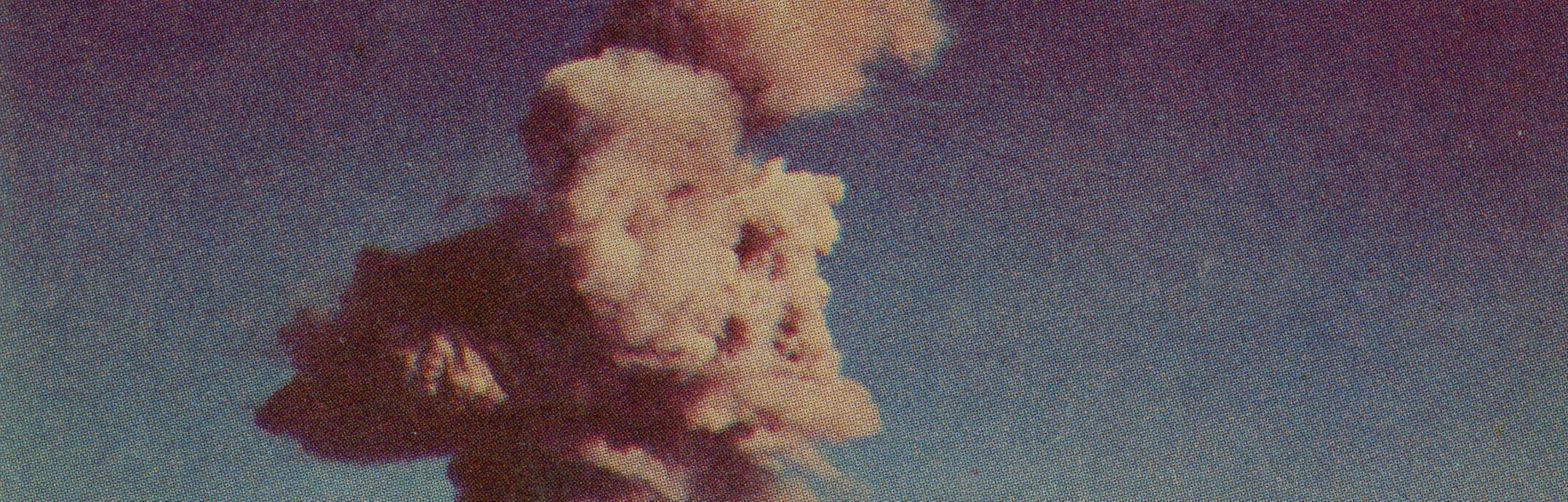 A photographic postcard shows an atomic cloud dissipating over an atomic detonation area, circa 1952...